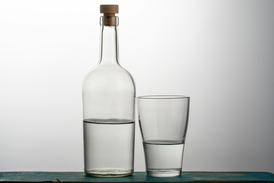 A clear glass bottle and tasting glass of water in a minimal setting